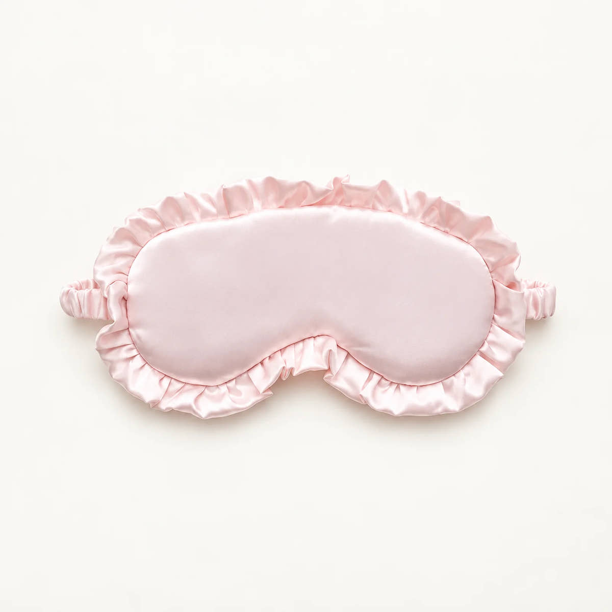 Light pink sleep eye mask with a satin finish, ruffled trim and gathered strap ends.
