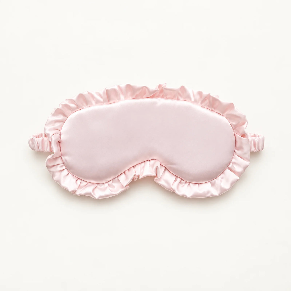 Light pink sleep eye mask with a satin finish, ruffled trim and gathered strap ends.
