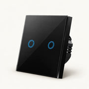 Black two-gang glass touch light switch with two blue circular controls on a warm off-white background.