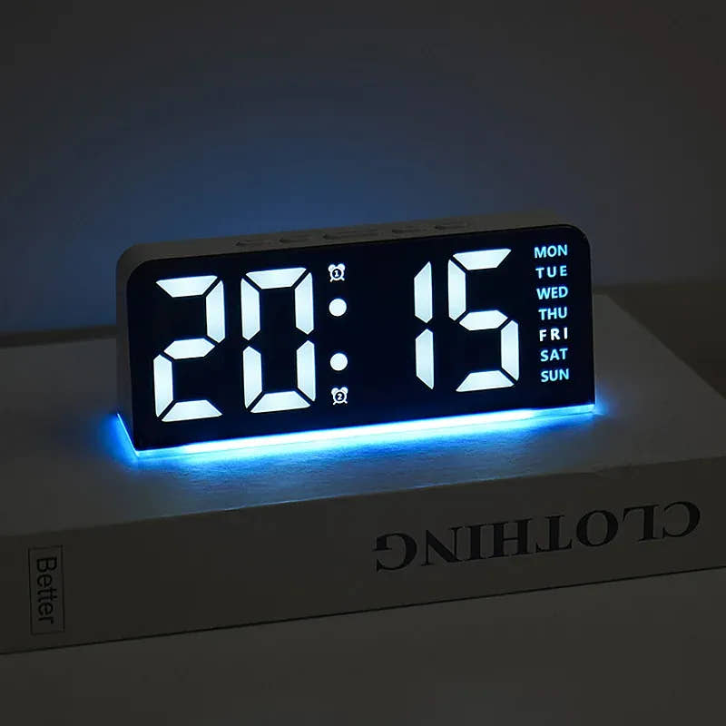 Black digital alarm clock with white digits and blue mood light on a bedside surface