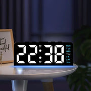 Digital alarm clock on a round bedside table beside a framed print