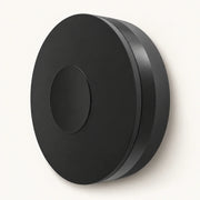Single black circular WiFi IR/RF remote hub shown at an angle on a warm off-white background.