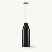 Handheld Milk Frother and Egg Whisk on a warm off-white background with a soft natural shadow.